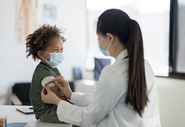 Female doctor places a band-aid on a young boy’s arm 