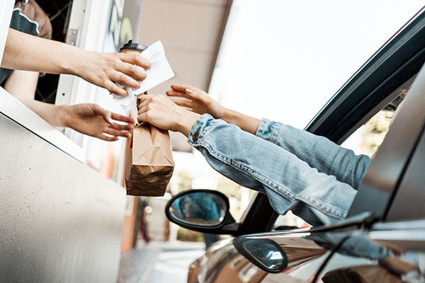 A customer reaching out of their car to collect food at a drive-through