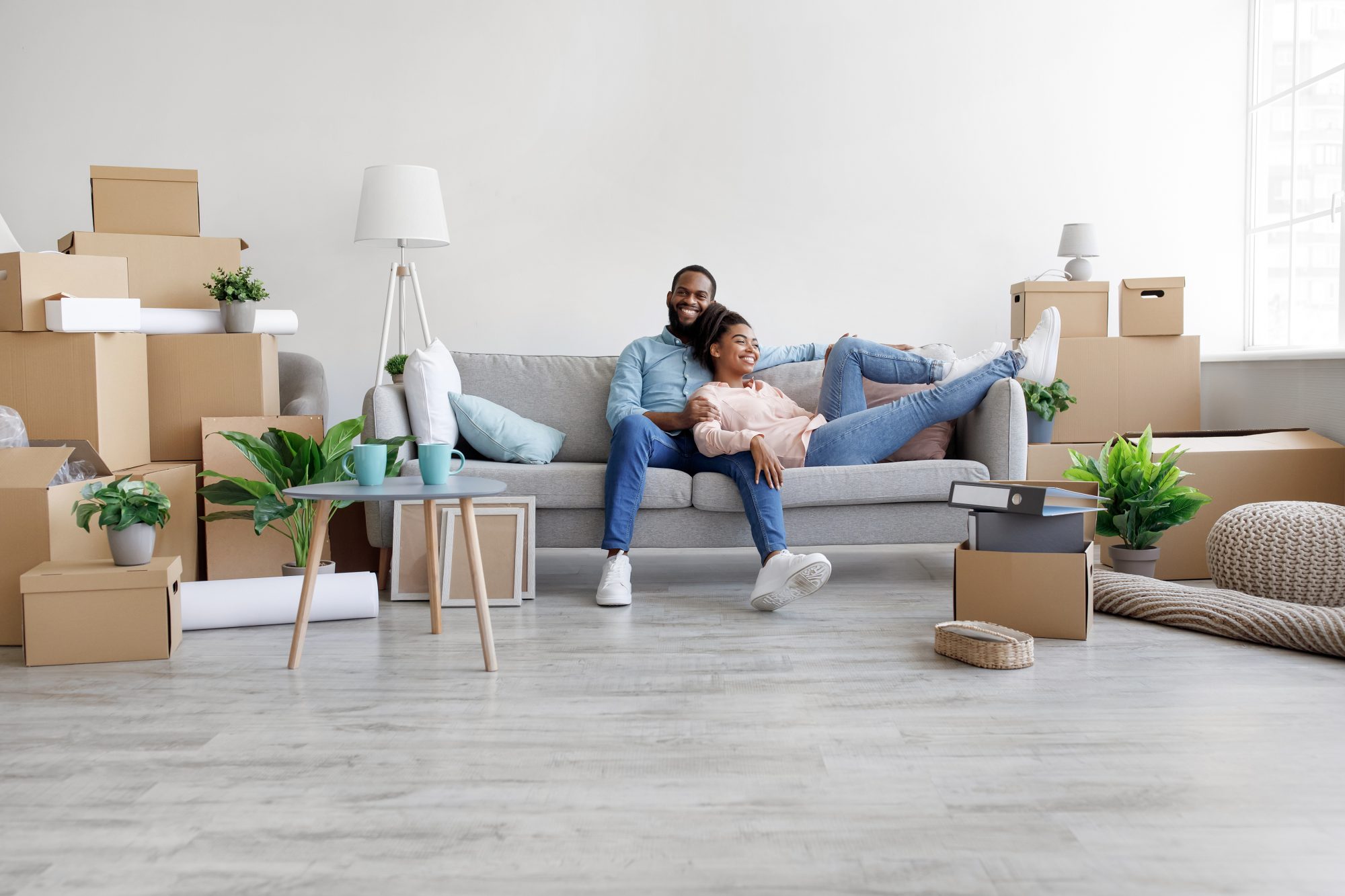 Young couple relaxing on couch in living room surrounded by unpacked moving boxes