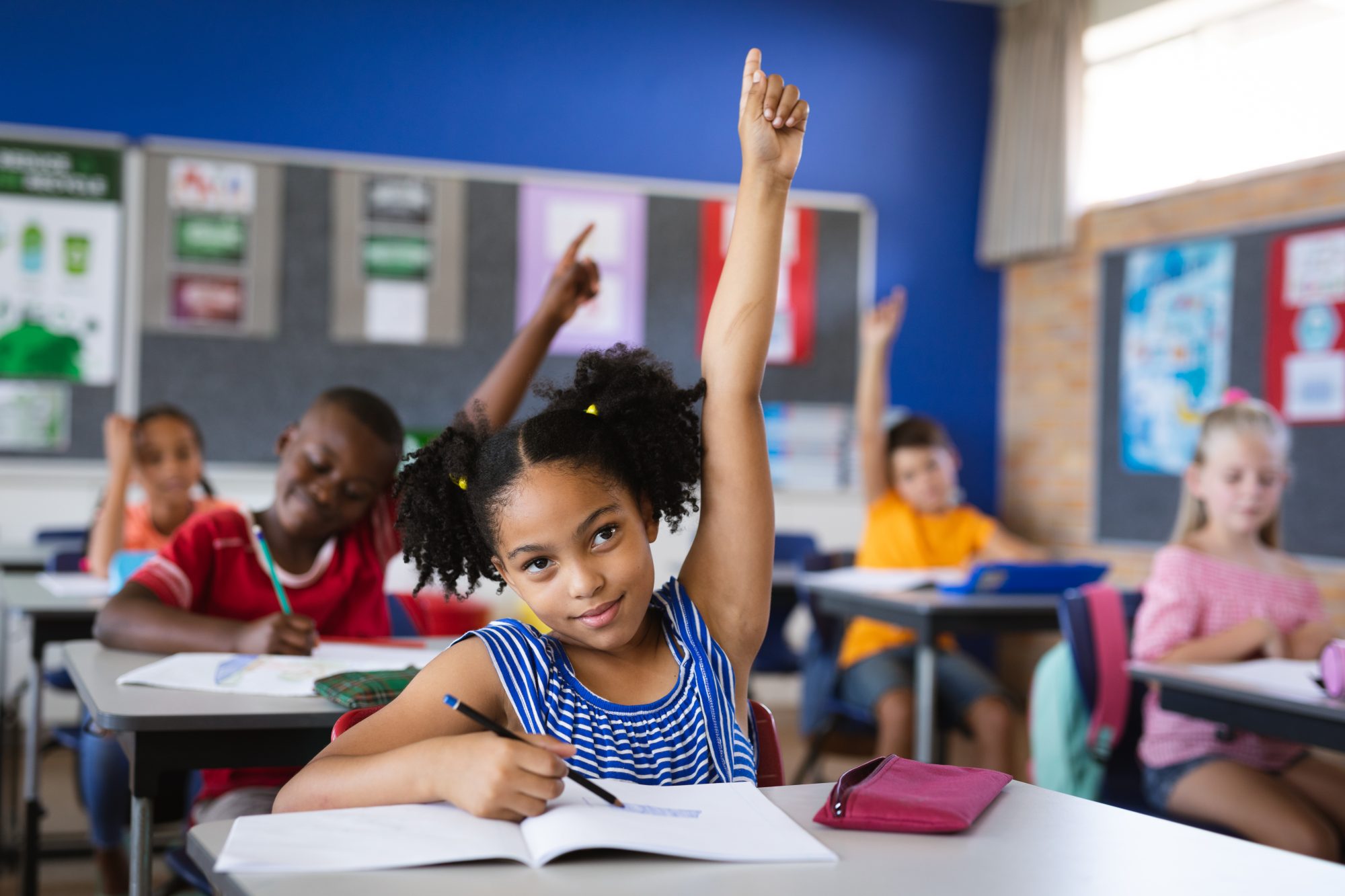 African American girl raising her hand while sitting on her desk in the class at school. 