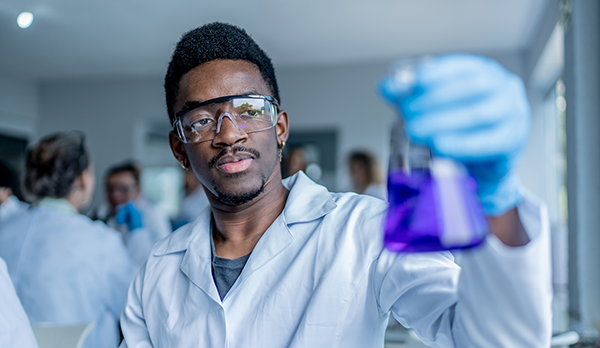 University STEM student in lab coat swirls liquid in a beaker.